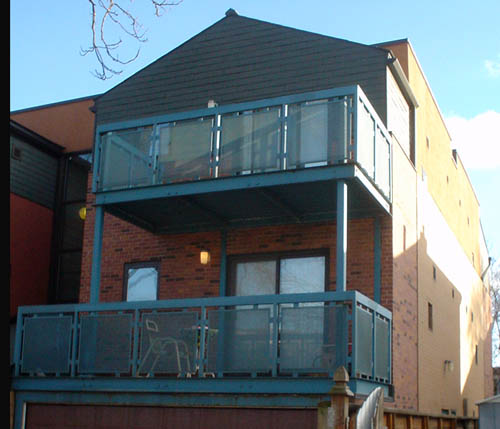 Upper two storeys of gabled brown brick building have blue grated balconies. Right-hand side is yellow- and cream-coloured with small windows