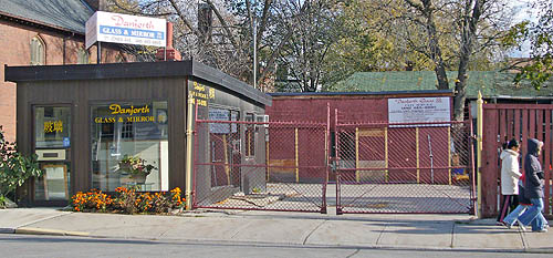 Squat rectangular building, almost a single room, is labelled Danforth Glass & Mirror and sits on a fenced-in paved yard