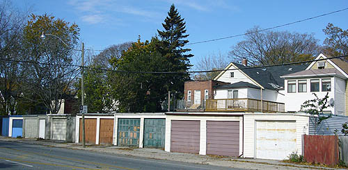 Garages with chipped paint in rust, green, purple, and white lead to a few two-storey houses