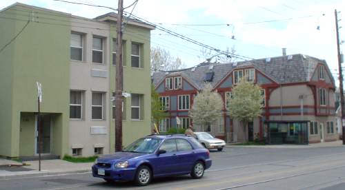 T-intersection shows green-and-cream stucco building on near corner and blue-and-burgundy mock-Tudor building on far corner