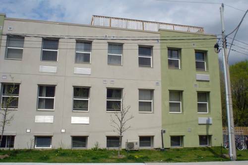 Two-storey stucco building, green at front, tan at rear, with short wooden deck railings on roof
