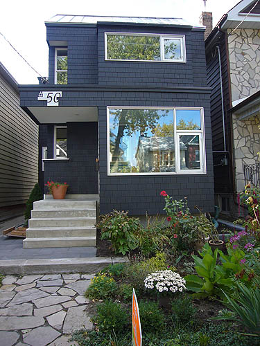 Black-shingled house with colour ful garden, inset side windows, and short concrete staircase