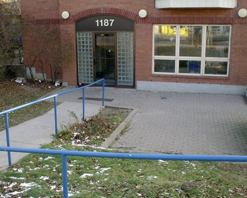Paved entrance sinks below ground level, with blue banister