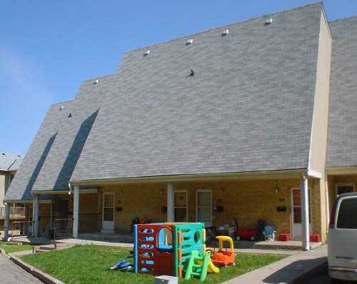 Three north-facing windowless roofs, each set back from the other. Children’s play sets sit on trapezoidal lawn area