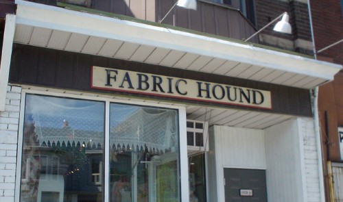 Black serif type reads FABRIC HOUND on a white sign with red border