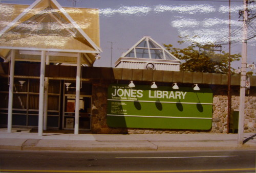 Stone building with giant green sign reading JONES LIBRARY and yellow canopy over entrance