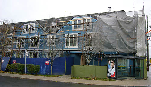 Blue building with latticework of scaffolding (including grey plastic tent covering an entire end)