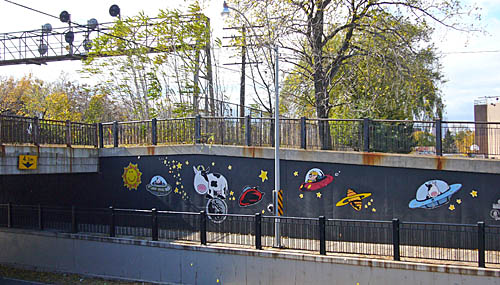 Black walls leading out of an underpass have bright paintings of flying saucers