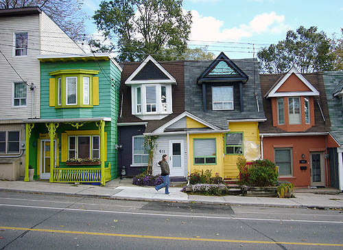 Two-storey row houses sit cheek by jowl: One green with yellow trim, one brick, onother brick with yellow-and-greentrim at ground level, one red brick