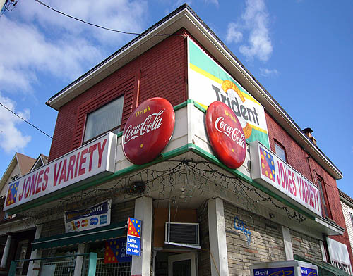 Brick building has sign reading JONES VARIETY in Arial, with three-dimensional Drink Coca-Cola badges at the ends of the sign boards
