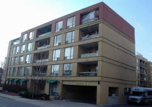 Bottom four storeys of building are buff brick, top floor red brick, with green awnings on some windows and a parking-garage entrance at ground floor
