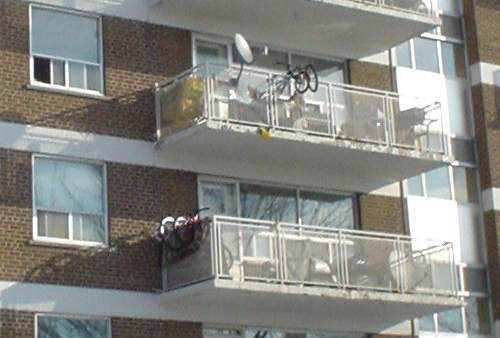 Two neighbouring balconies have satellite dishes, one lying on the balcony floor, another attached to the railing
