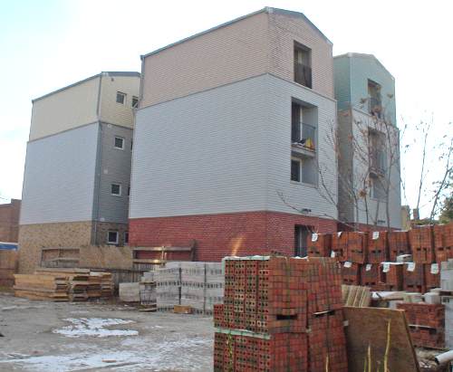 Three-storey building is divided into four pods, each with a peaked roof, a brick base, and a middle half and top quarter all in different pastel colours of siding