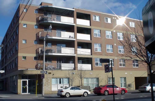 Five-storey building has buff brick on ground floor, brown brick elsewhere, with balconies that curve on their inset edges