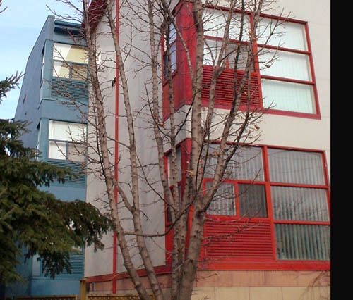 Windows are surrounded in red against cream-coloured building, with blue mass projecting leftward at rear