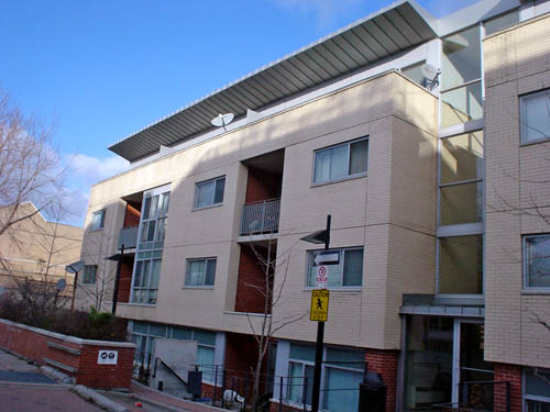 Buff-brick four-storey building has aluminum awning on its recessed top level and red-painted inset balconies on the first three floors