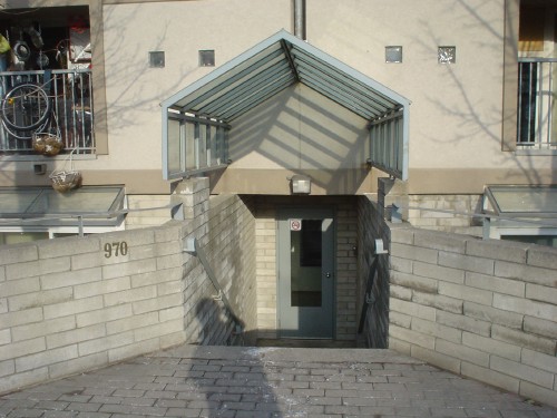 Sunken single-door entrance flanked at ground level by angled grey-brick retaining walls, one of them labelled 970