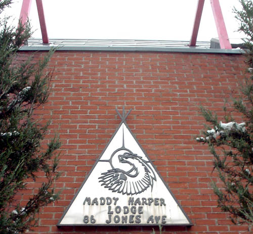 Sign in the shape of a teepee (with faux twigs at the apex) shows an eagle and MADDY HARPER LODGE 86 JONES AVE. in faux-handwritten type