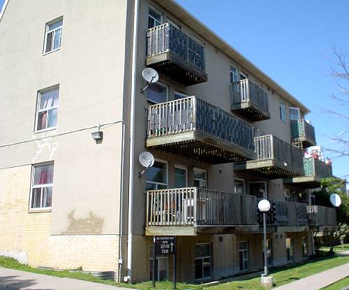 Three-storey building has wooden-slat balconies of diminishing size on each floor, three satellite dishes, and a nearby light standard