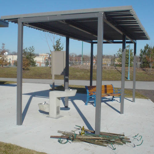 Shelter with no walls and a wood-slat roof covers a park bench and fountain