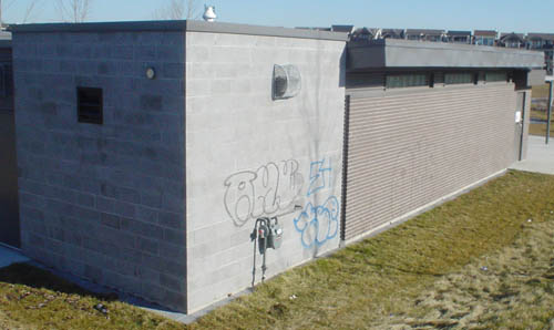 Single-storey building has concrete end (with graffiti) and brown-brick extension with shrt eaves