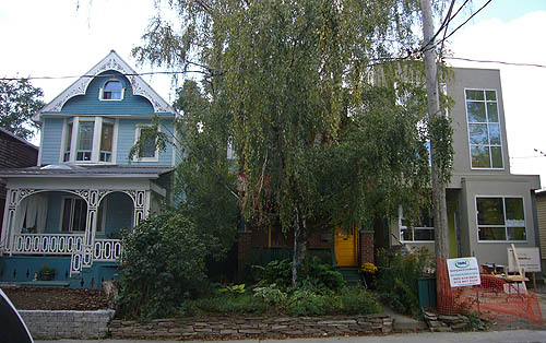 Three houses on a street: One in baby blue with gingerbread trim, another obscured by a willow tree, and a beige modernist construct