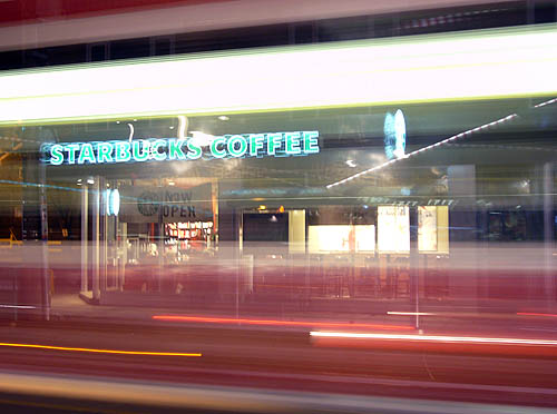 Blurred red and white streaks leave signs reading STARBUCKS COFFEE and NOW OPEN visible